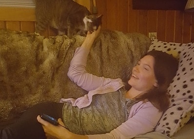 Woman lying on couch pets cat standing above her.